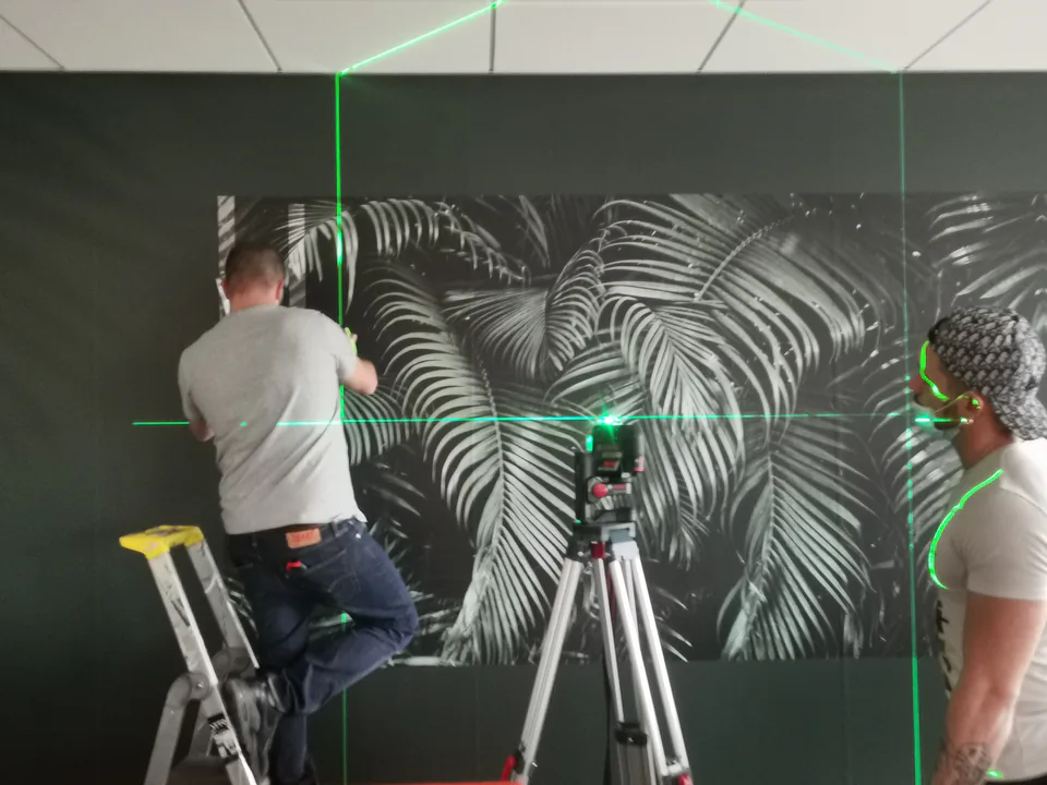 Deux poseurs Paristic installent un papier peint de palmes au niveau laser