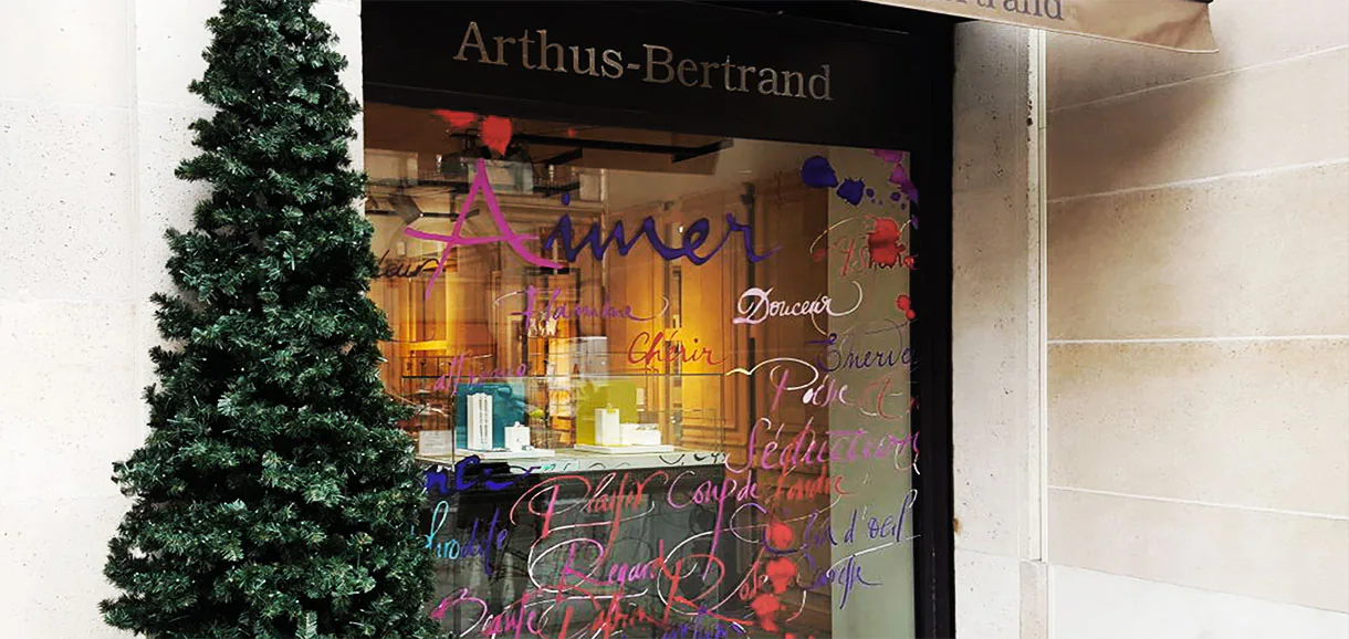 Façade Arthus-Bertrand et sapin de Noël devant une vitrine couverte de mots manuscrits en adhésif découpé