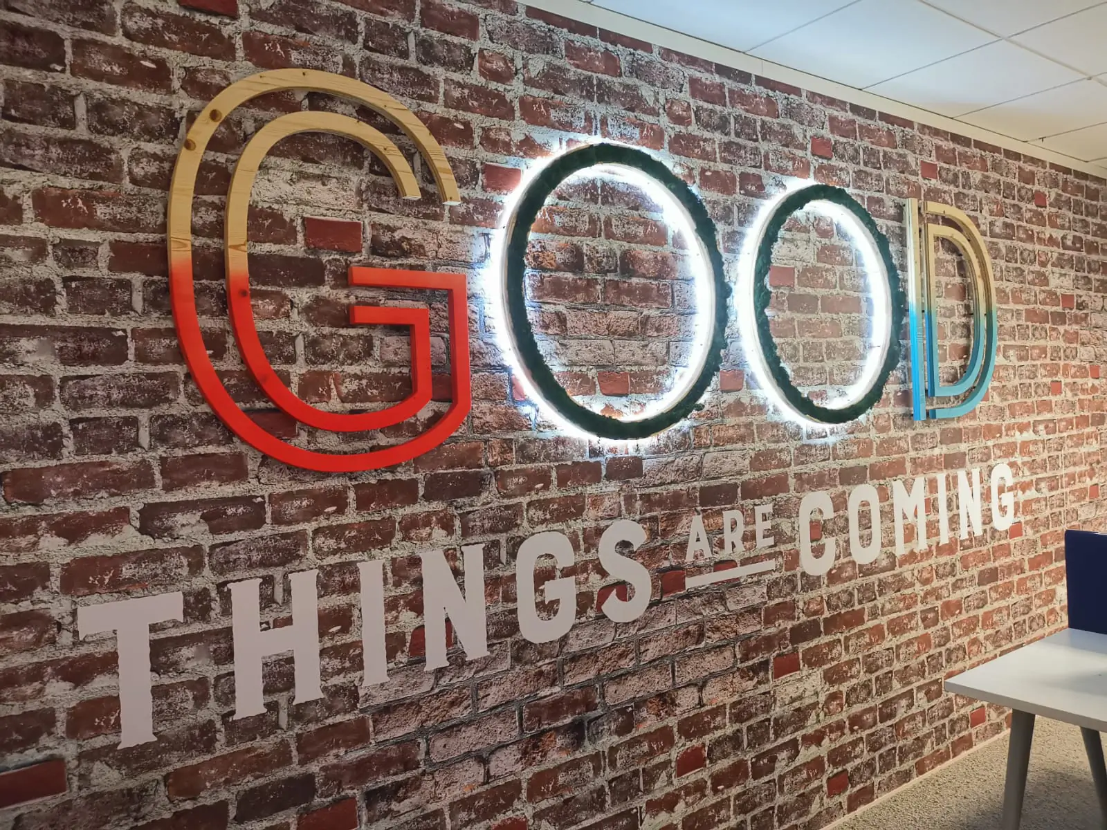 Lettrage lumineux « Good things are coming » sur papier peint brique, open space AXA Banque