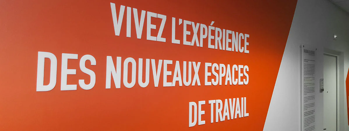 Mur orange des bureaux BNP Real Estate avec lettrage en relief blanc « Vivez l'expérience des nouveaux espaces »