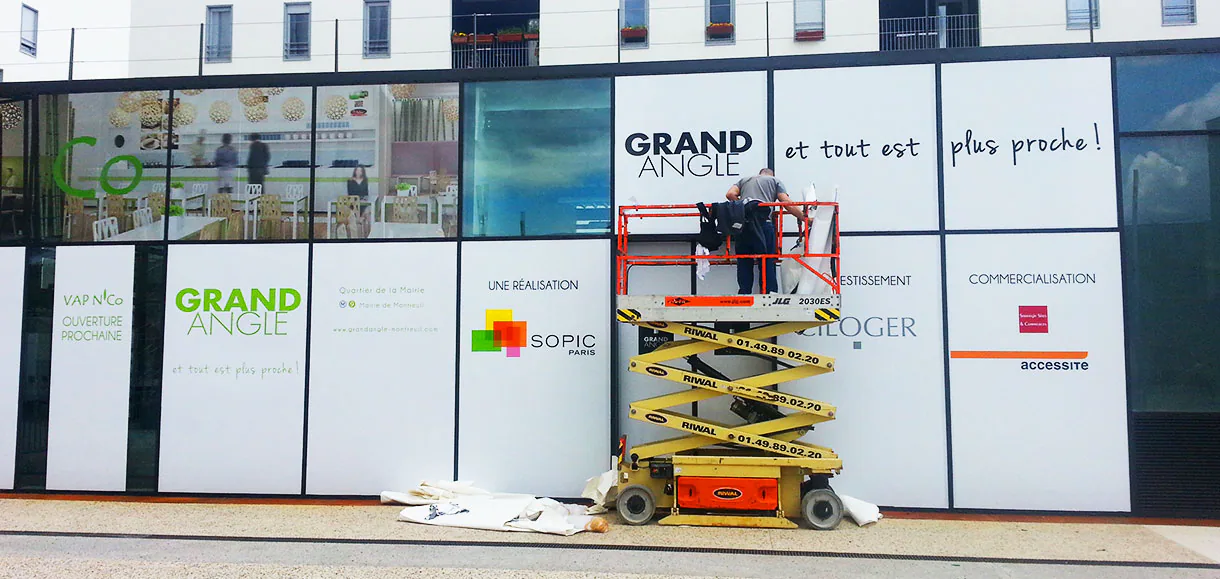 Pose d'adhésifs microperforés sur une vitrine depuis une nacelle élévatrice au centre commercial de Montreuil