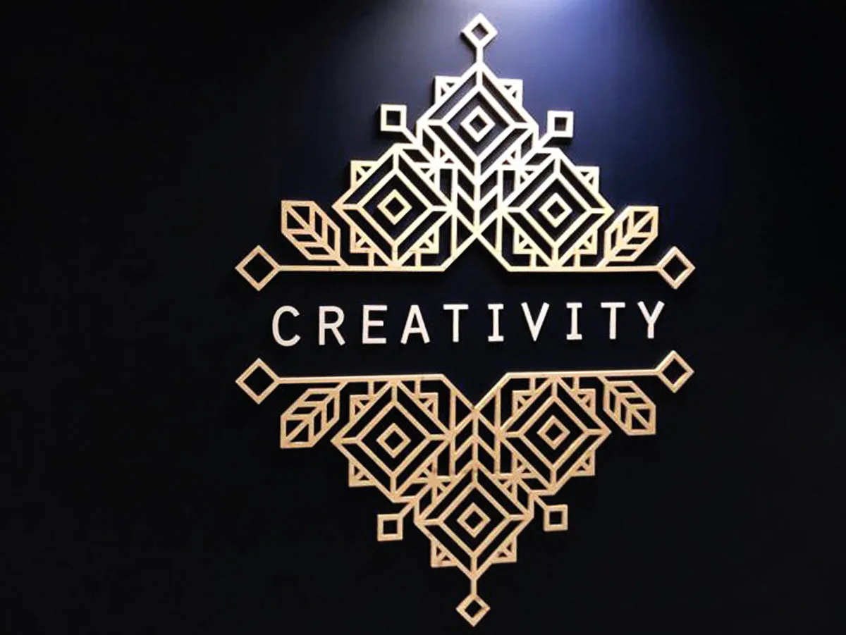 Motif art déco doré et lettrage Creativity découpés, posés sur un mur bleu nuit de bureaux d'une compagnie d'assurances