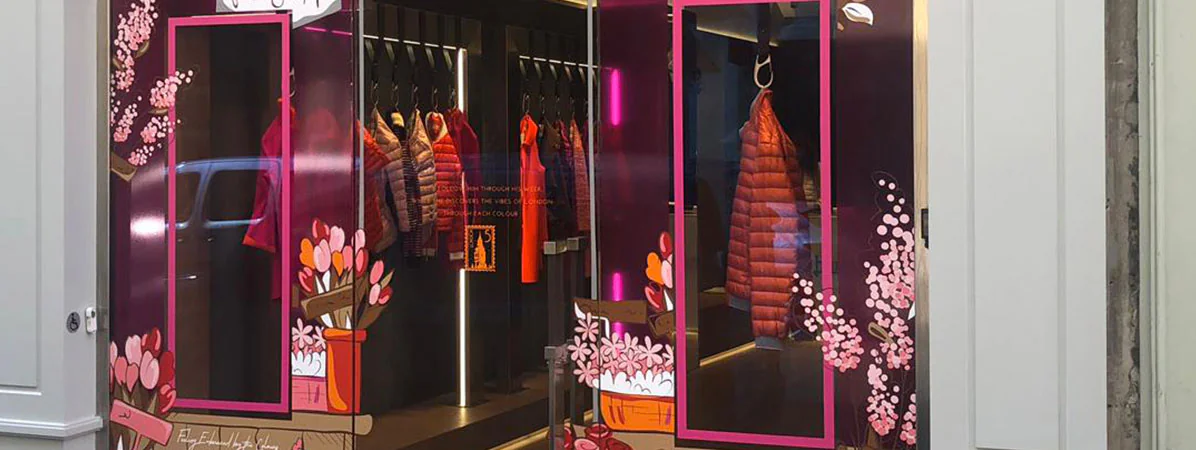 Vitrine Herno rue Saint-Honoré habillée d'une vitrophanie fleurie rose et violette autour des doudounes exposées