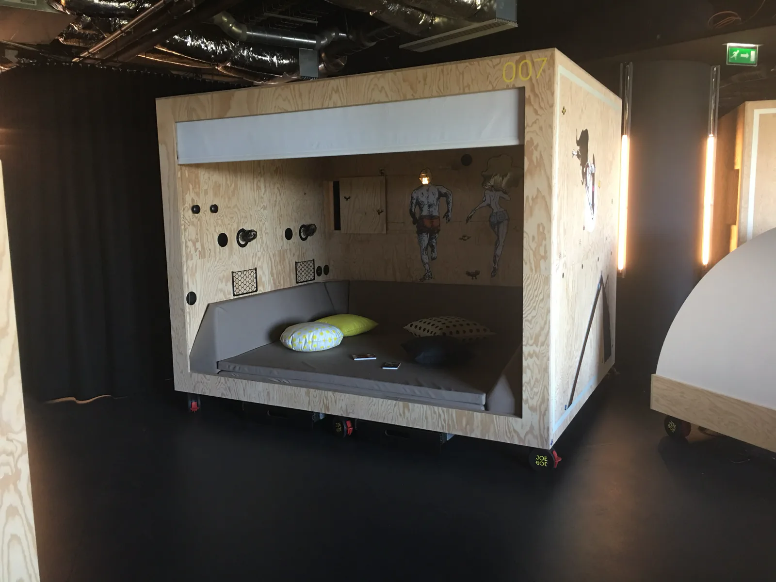 Cabine couchette en bois de l'hôtel Jo&Joe ornée de visuels street art en adhésif, dans un espace commun sombre