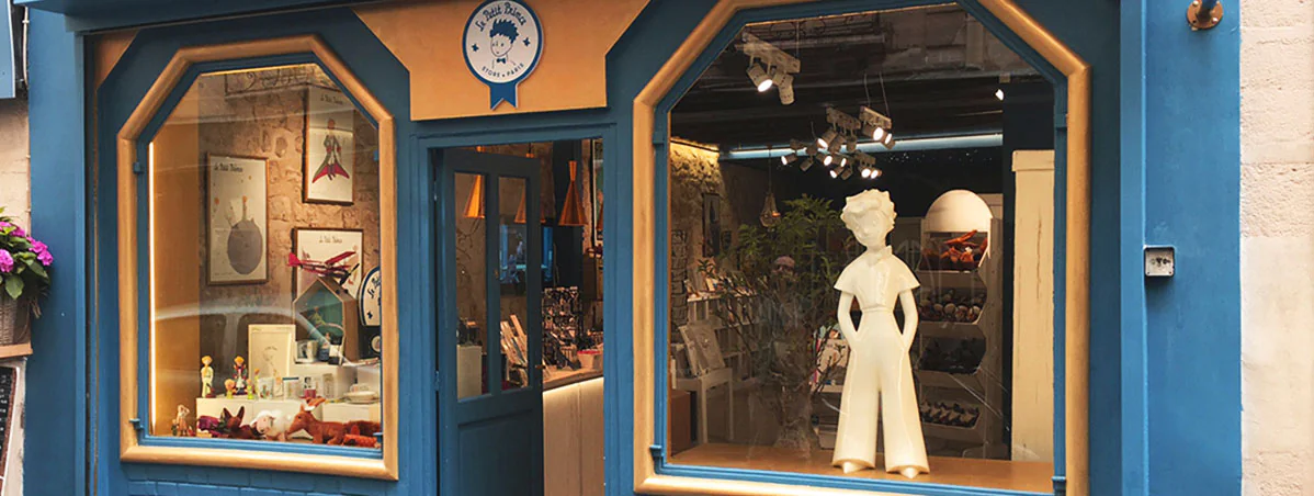 Façade bleue de la boutique Le Petit Prince : vitrines éclairées et statue blanche du personnage, projet Paristic
