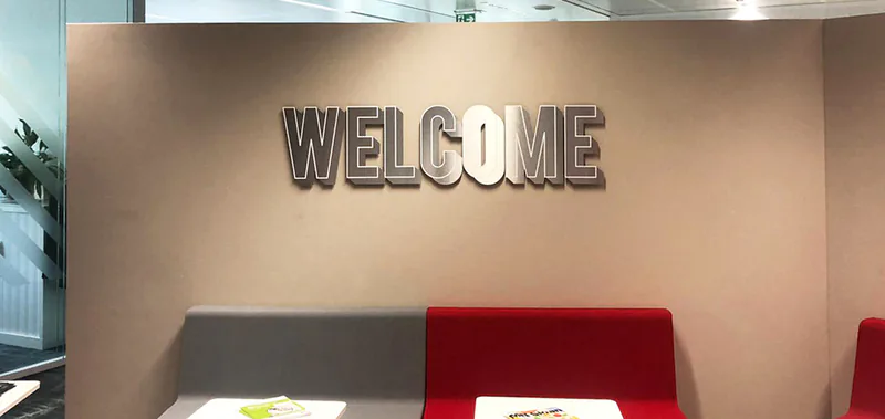 Accueil des bureaux SNCF : lettrage Welcome en relief aluminium sur mur taupe au-dessus de banquettes rouge et grise