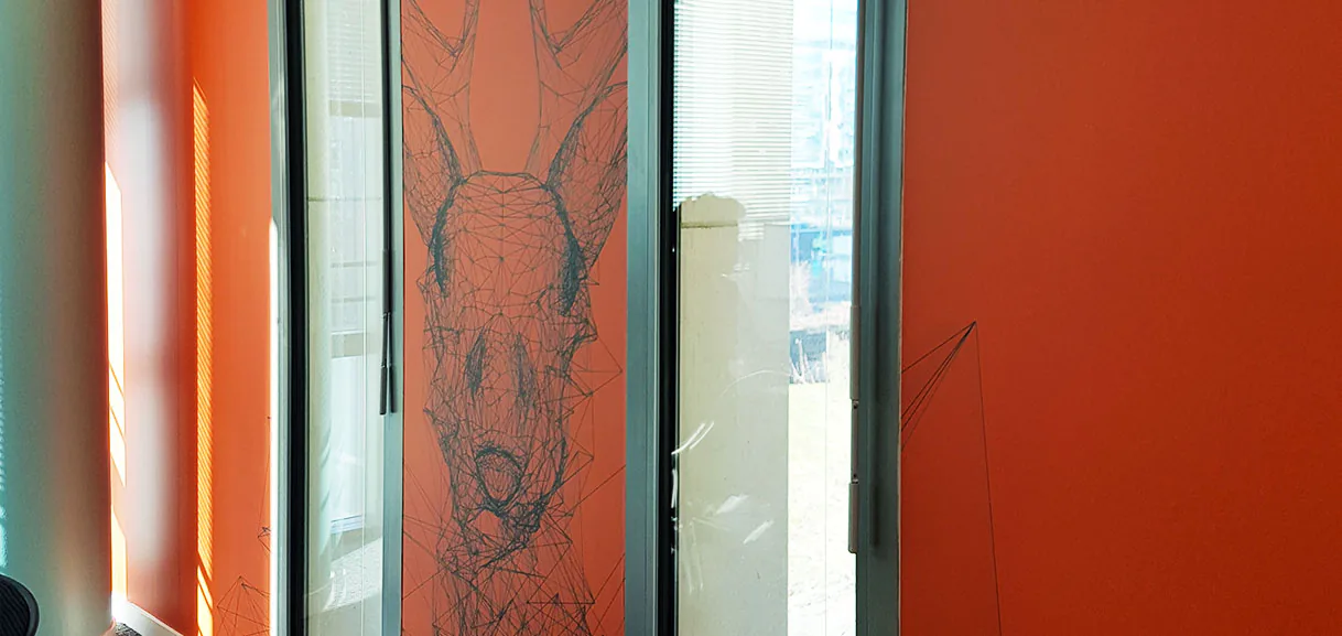 Tête d'animal stylisée en adhésif sur mur orange entre deux fenêtres, décoration murale des Terrasses de l'Arche