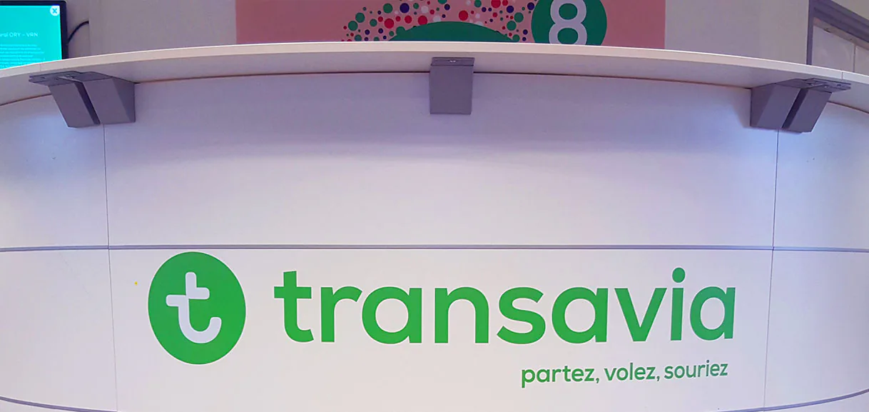 Banque d'accueil Transavia habillée du logo et du slogan de la compagnie en adhésif vert, signalétique Paristic