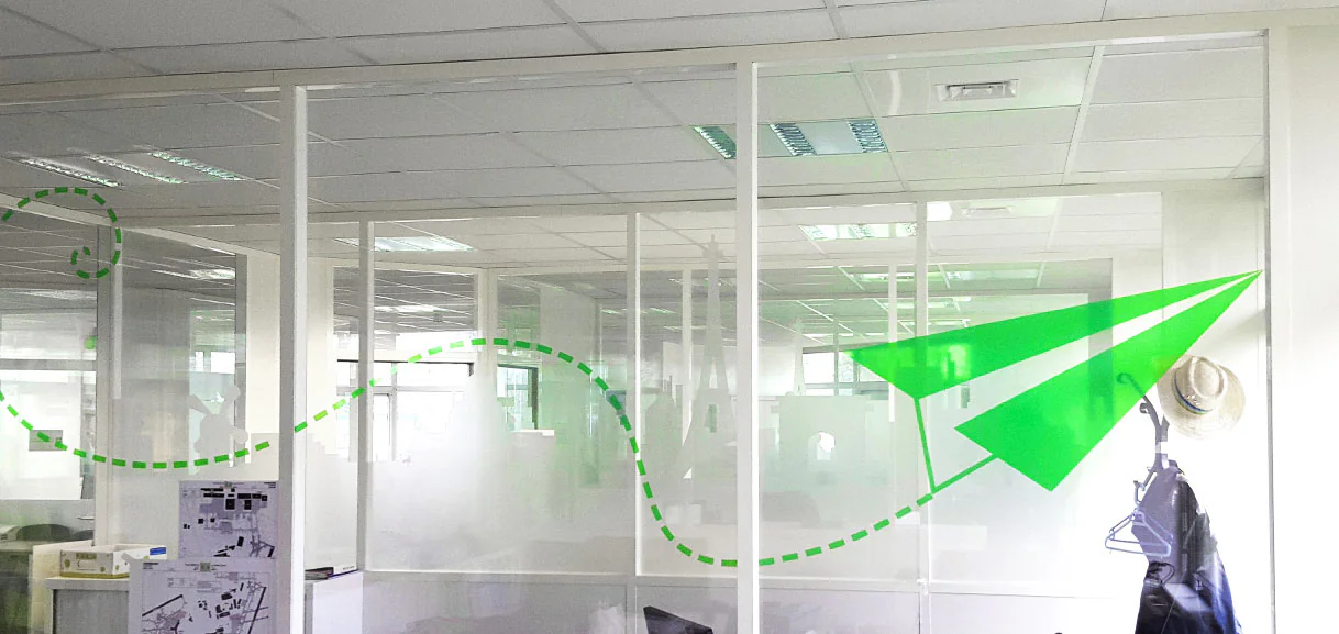 Cloisons vitrées des bureaux Transavia : vitrophanie d'avion en papier vert et trajectoire en pointillés