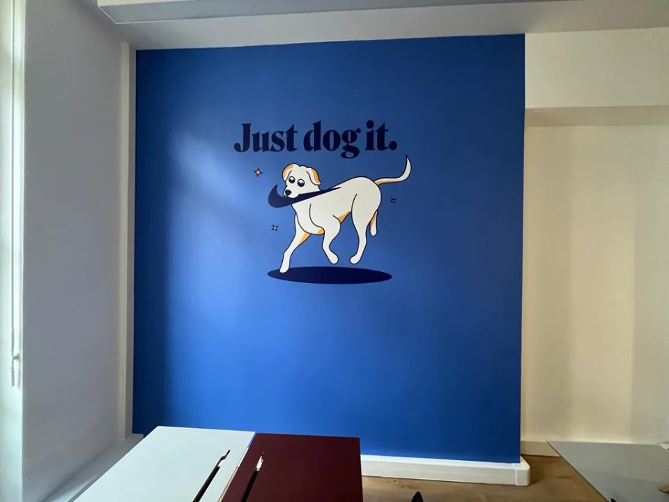 Décoration murale bureau : mur bleu habillé d'une illustration de chien blanc et du slogan « Just dog it. », réalisation pour Dalma