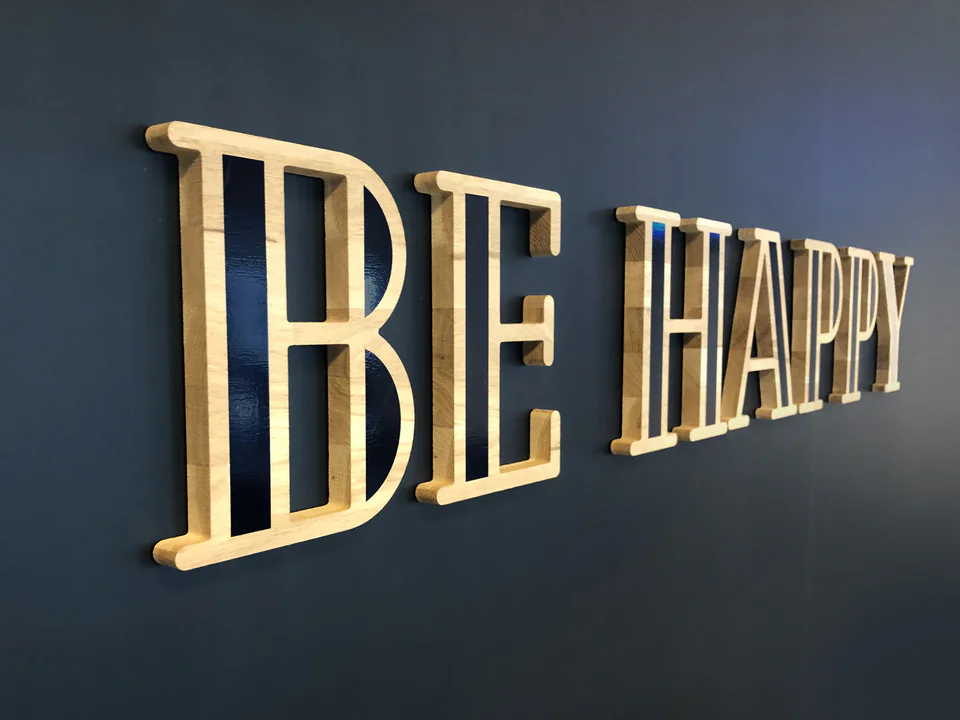 Lettrage en bois massif « Be Happy » en relief sur un mur bleu nuit