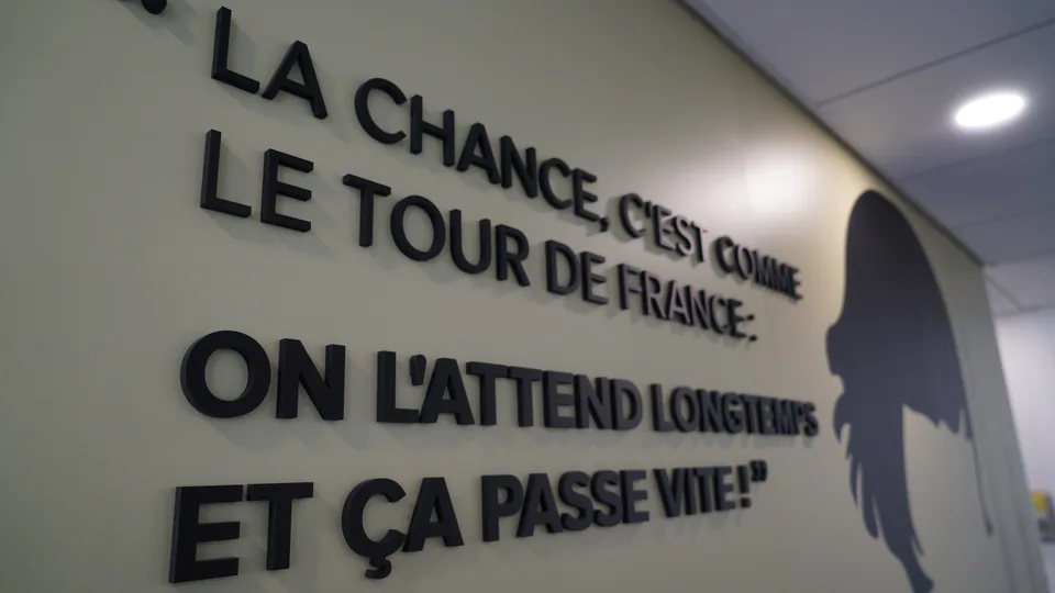Gros plan sur des lettres en relief noires d'une citation murale, silhouette en arrière-plan