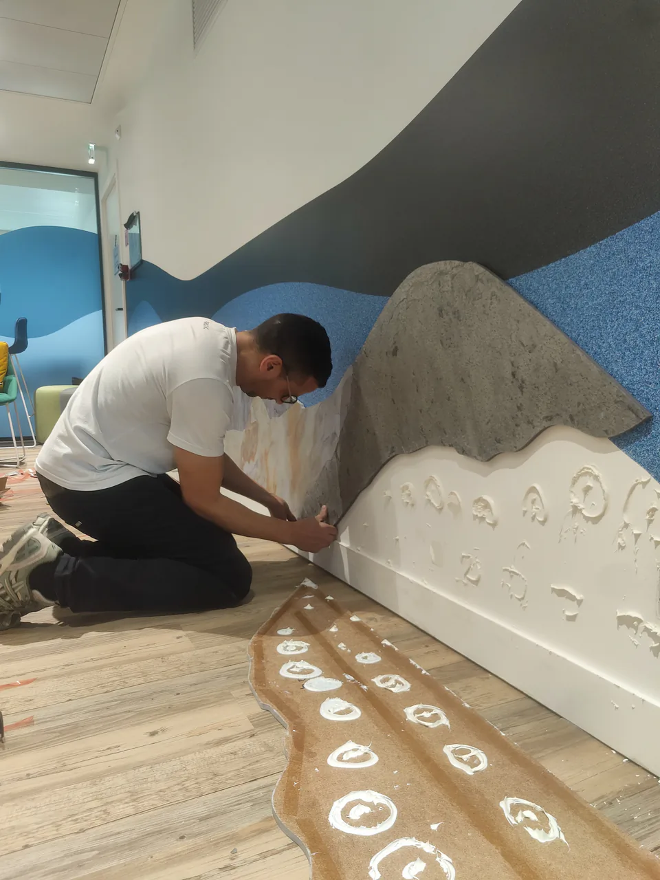 Technicien Paristic posant à genoux un relief mural façon montagne sur un décor bleu et gris