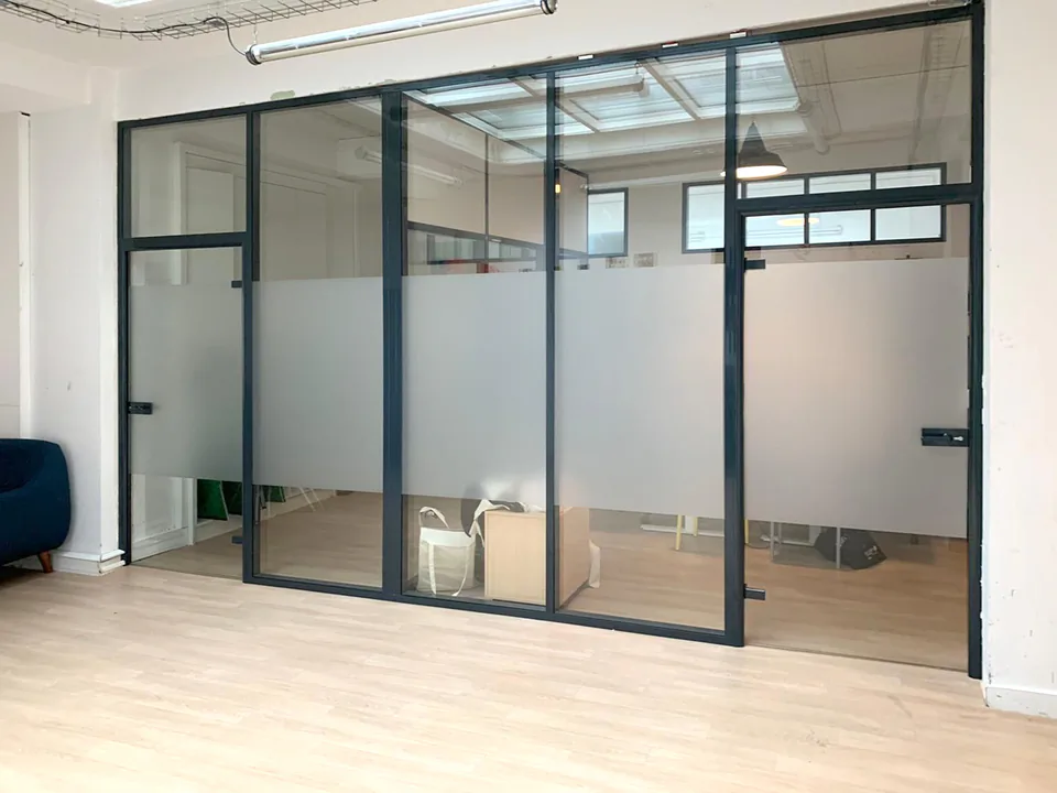 Verrière de bureau avec film dépoli en partie basse et vue sur un immeuble ancien à travers le haut vitré