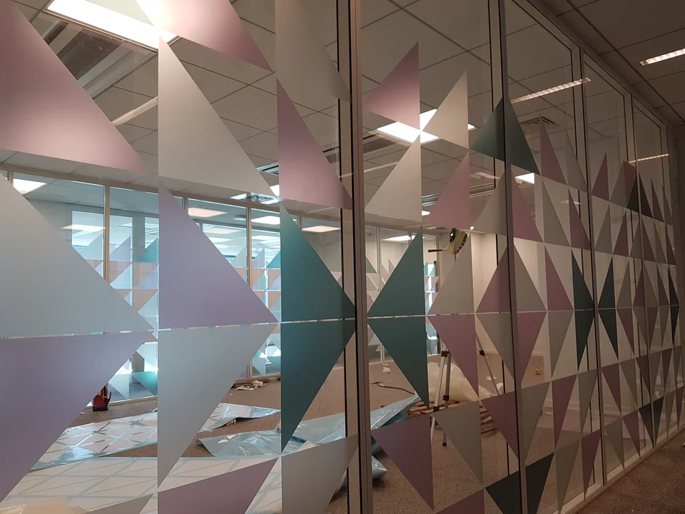 Cloison vitrée de bureau habillée d’un motif géométrique de triangles pastel en vitrophanie