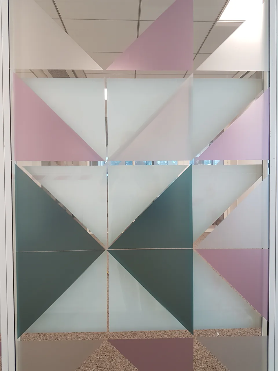 Vitrophanie à triangles roses, verts et blancs sur une paroi vitrée de bureau, vue de face