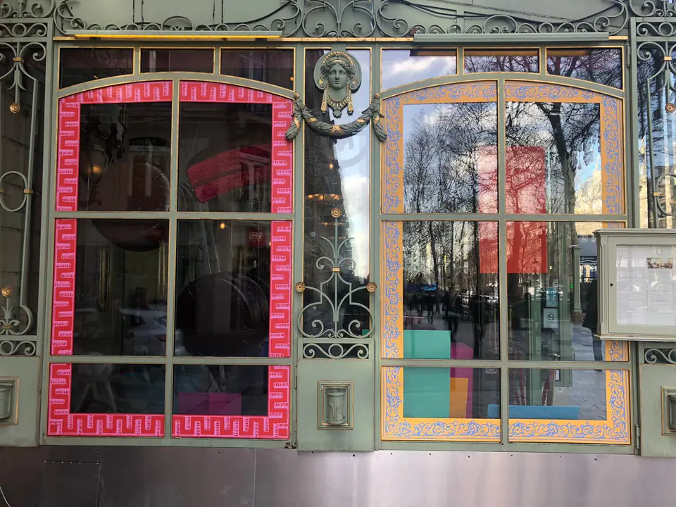 Façade parisienne ouvragée avec un cadre vitrophanie rouge à motifs et un cadre bleu et or